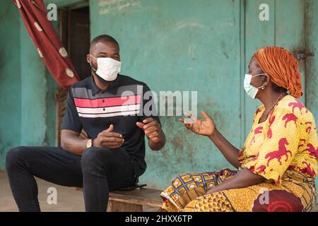 Eine ältere afrikanische Frau und ein junger Mann, der medizinische Masken trägt und sich unterhält Stockfoto