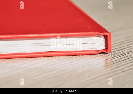 Nahaufnahme eines neuen geschlossenen roten Buches auf einem Holztisch. Literatur, Bildung, Lesekonzept. Stockfoto