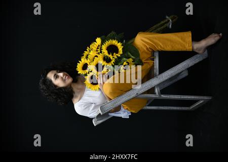 Vertikale Aufnahme einer hispanischen Hündin, die vor einem schwarzen Hintergrund mit Sonnenblumen posiert Stockfoto