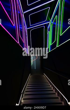 Beleuchtete Treppe mit Neonlinien an Wänden und Decke. Eintritt zur Disco-Nachtparty. Nachtleben in der Stadt. Stockfoto