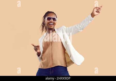 Fröhliche und fröhliche, unbeschwerte, dunkelhäutige junge Frau, die Spaß am Tanzen auf beigem Hintergrund hat. Stockfoto