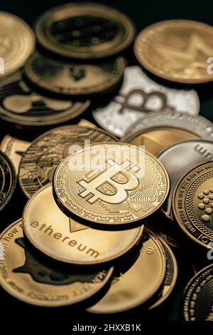 Nahaufnahme eines goldenen Bitcoins in einem Stapel, unter anderem verschiedener digitaler Kryptowährungen. Stockfoto