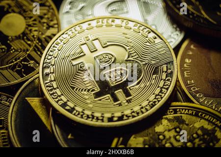 Nahaufnahme eines goldenen Bitcoins in einem Stapel, unter anderem verschiedener digitaler Kryptowährungen. Stockfoto