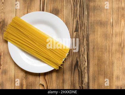 Rohe Spaghetti, Pasta auf weißem Teller auf dunklem Holzgrund. Stockfoto