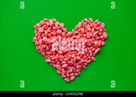 Kieselstein rotes Herz mit kleinen dekorativen Steinen auf grünem Hintergrund ausgelegt. Konzept der Liebe, Romantik und valentinstag. Stockfoto