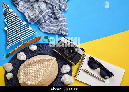 Reisetasche aus Leder, Strohhut, Nackentuch, Notebook, Vintage-Kamera, Muscheln und Segelyacht auf gelbblauem Hintergrund. Reiseausrüstung. Obere V Stockfoto