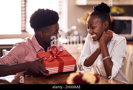 Ich habe das schon seit Tagen versteckt. Kurzer Schuss eines liebevollen jungen Mannes, der seiner Frau am Valentinstag zu Hause ein verpacktes Geschenk übergab. Stockfoto