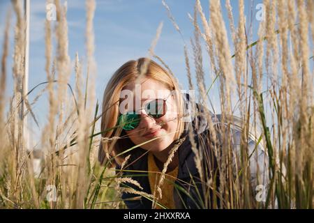 Porträt einer attraktiven Frau in Sonnenbrillen auf dem Feld voller trockener gelber Stängel Stockfoto