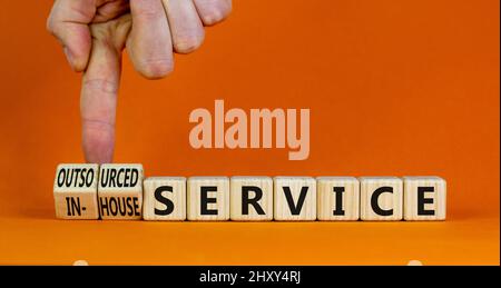 Symbol für internen oder ausgelagerten Service. Der Geschäftsmann verwandelt sich in Würfel und ändert die Worte des Inhouse-Services in den Outsourcing-Service. Orangefarbener Hintergrund. Unternehmen I Stockfoto