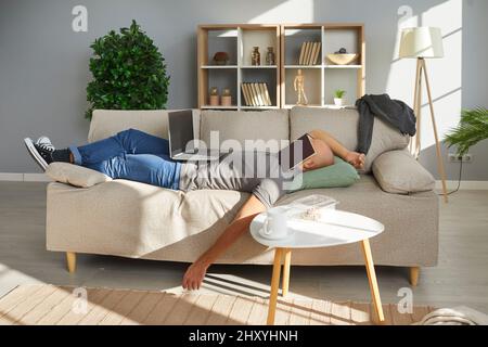 Müde fauler Student, der zu Hause studiert, schläft mit Buch auf seinem Gesicht ein Stockfoto