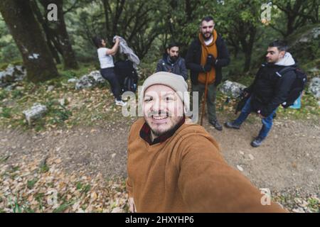 Junger Kaukasusmann, der ein Selfie einer Gruppe von Wanderern auf einem schmalen Pfad im Wald ausruhte Stockfoto