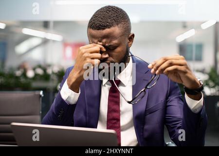 Nahaufnahme eines erschöpften schwarzen Managers, der im Büro sitzt und Kopfschmerzen hat Stockfoto