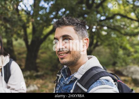 Nahaufnahme eines kaukasischen Mannes, der einen Rucksack trägt und unter hellem Sonnenlicht auf einem Wald steht Stockfoto