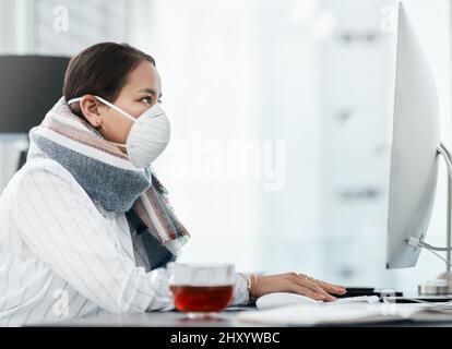 Überleben der fokussierten. Aufnahme einer maskierten jungen Geschäftsfrau, die in einem modernen Büro einen Computer benutzt. Stockfoto