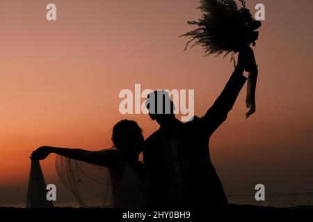Silhouette eines Paares, das während des Sonnenuntergangs einen Blumenstrauß hält Stockfoto