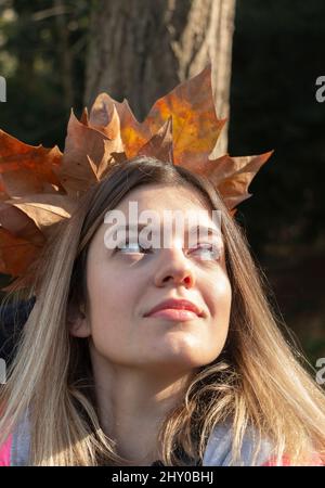 Frau, die Herbstblätter im Wald hält, lächelt glücklich und aufgeregt. Portrait des Mädchens mit bunten Blättern. Laub im Wald. Frau in einem modischen Mantel. Stockfoto