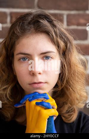 Frau Gesicht und Hände gefaltet in Gestik des Flehens in gelb gemalt - blau . Beendet den Krieg. Hoffnung und Glaube. Stolz der ukrainischen Nation. Bleib witzig Stockfoto