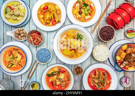 Set aus süßen Thai-Gerichten mit würzigem, geschmortem Huhn, farbigem Reis, Schweinefleisch-Eintopf, Gewürzen, Essstäbchen, Limette und Chilischoten Stockfoto