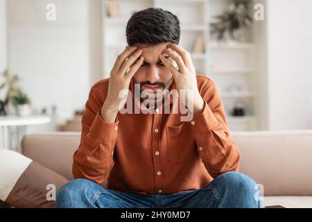 Gestresster arabischer Mann sitzt auf der Couch und denkt nach Stockfoto