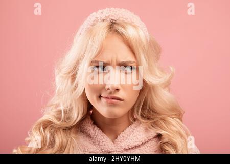 Verärgert nachdenkliche Frau, die beiseite schaut, sich etwas vorstellt, sich zweifelnd oder verärgert fühlt, rosafarbener Studiohintergrund Stockfoto