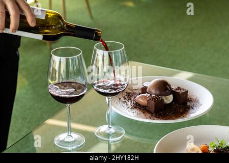 Eine Person, die Rotwein in ein Glas neben einem Schokoladendessert auf einen Teller gießt. Stockfoto