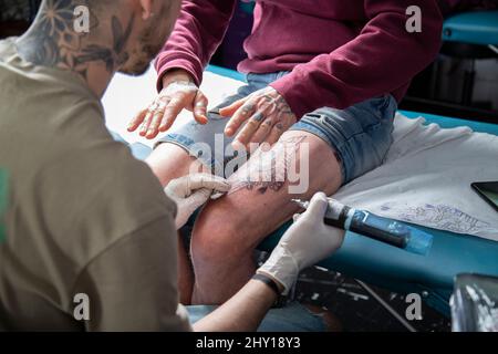 Crop anonymen Meister macht Tattoo auf Bein von nicht erkennbaren Kunden mit speziellen Rotary Tattoo Maschine während der Arbeit in professionellen Salon Stockfoto
