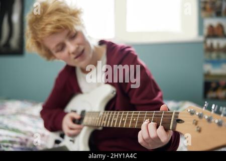 Teenage Girl Sitzend Auf Dem Bett Lernen Zu Spielen E-Gitarre Im Schlafzimmer Stockfoto