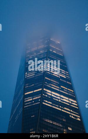 Von unten befindet sich ein modernes Hochhaus mit glühenden Fenstern, das sich am Abend vor dem nebligen Himmel in New York City befindet Stockfoto
