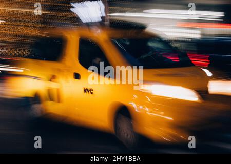 Unscharfes gelbes Taxi mit leuchtend leuchtenden Scheinwerfern, die nachts auf einer dunklen Straße in New York City in Bewegung fahren Stockfoto