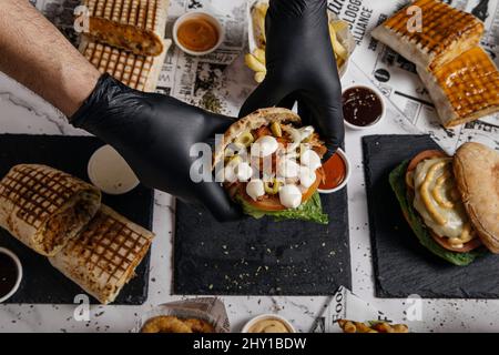 Von oben der Ernte anonymen männlichen Koch in Handschuhen zeigt köstliche griechische Gyros mit Mozzarella und Oliven über dem Tisch mit Shawarma Stockfoto