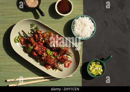 Blick von oben auf köstliche marinierte Hähnchen auf Spieße mit Gemüse auf dem Tisch serviert mit Schüsseln von Reis, Sojasauce, Sesam und Lauch im Restaurant Stockfoto
