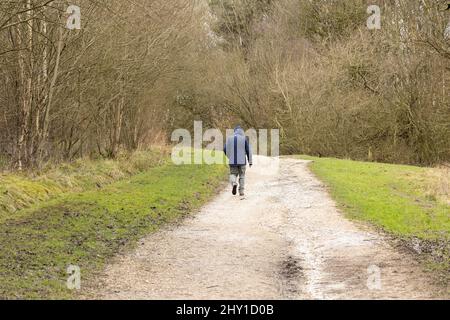 Ein eingefleischter Mann mit Kapuzenpullover, der in der Winterlandschaft entlang einer Feldbahn spazierengeht Stockfoto