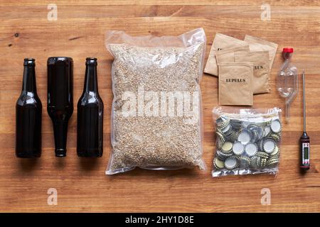 Draufsicht Layout von Glasflaschen und Paket von Gerstenkörnern für die Herstellung von hausgemachtem Bier auf dem Tisch mit Lupulus und Metallkappen Stockfoto