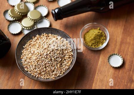 Draufsicht auf Glasflaschen in der Nähe einer Schüssel mit Gerstenkörnern und Metallkappen auf dem Tisch für die Herstellung von hausgemachtem Bier Stockfoto