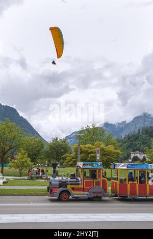 Vertikale Aufnahme eines fliegenden Gleitschirms und Touristen im kleinen Zug in Interlaken Schweiz Stockfoto