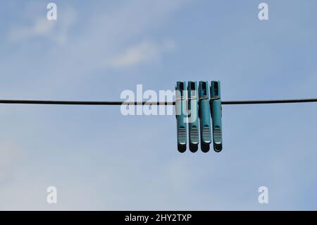 Alte, blau gefärbte Plastikkleidernadeln, die vom Draht am wolkigen blauen Himmel hängen Stockfoto