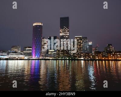 Blick auf die Ufergebäude von Canary Wharf, die sich in der Nacht auf der Themse spiegeln Stockfoto