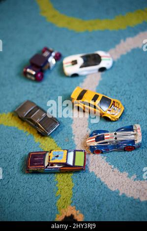 Selektive Fokusaufnahme einer Variation von Spielzeugautos der Marke Mattel Hot Wheels auf einem farbenfrohen Teppichboden Stockfoto