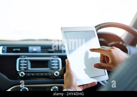 Vorbereitung auf die Arbeit auf dem Weg zur Arbeit. Ausgeschnittene Aufnahme eines nicht identifizierbaren Mannes, der ein digitales Tablet benutzt, während er ein Auto fährt. Stockfoto