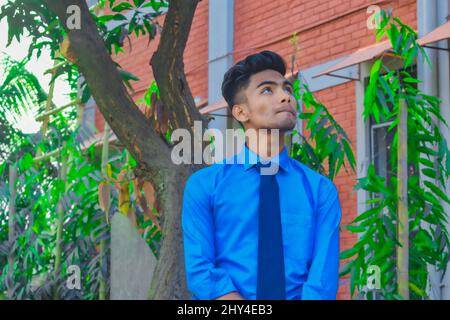 Junger, hübscher Mann mit blauer Krawatte und Hemd in einem Garten Stockfoto
