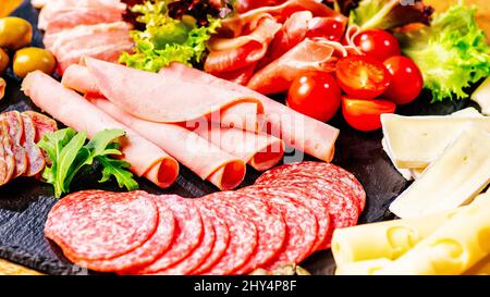 Auswahl an Wurstwaren und Würsten, Oliven und Gewürzen.Vorspeise aus Fleisch.verschiedene Sorten von Würsten mit Tomaten auf schwarzem Tisch serviert Stockfoto