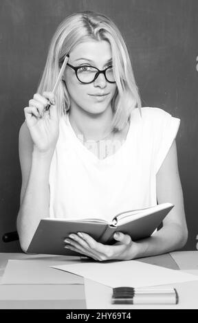 Studentin, die sich Notizen aus einem Buch in der Bibliothek gemacht hat. Lehrerin, die an ihrem Arbeitsplatz sitzt und Englisch unterrichtet. Denkkonzept Bildung. Ernst Stockfoto