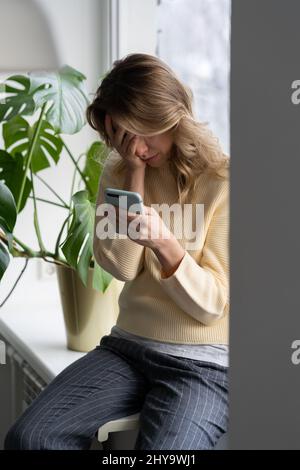 Depressive Frau mittleren Alters weint hält Smartphone lesen unangenehme sms empfangen schlechte Nachrichten zu Hause. Stockfoto