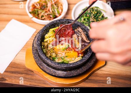 Bibimbap in einer schwarzen, beheizten Steinschüssel, koreanisches traditionelles Gericht - Bibimbap gemischter Reis mit Gemüse umfassen Rindfleisch und Spiegelei, japanisches Hot Pot Essen Stockfoto