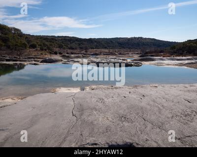 Pool von klarem Wasser mit Kalkstein im Vordergrund im Pedernales River mit einem Sandstrand und Kalksteinfelsen im Pedernales Falls State Park Stockfoto