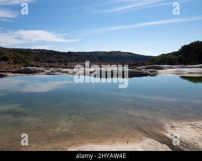 Pool von klarem Wasser mit Reflexionen im Pedernales River mit einem Sandstrand und Kalksteinfelsen im Pedernales Falls State Park in Texas Stockfoto