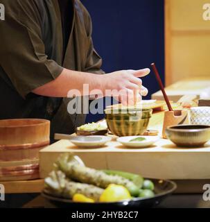 Küchenchef in schwarzer Uniform macht Nigiri-Sushi an der Sushi-Bar. Stockfoto