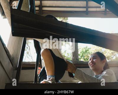 Mutter hilft ihrer Tochter, die Treppe zum Turm auf dem Spielplatz zu erklimmen. Freizeitaktivitäten für Familien im Freien. Stockfoto