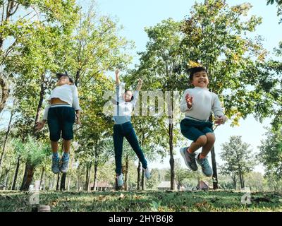 Zwei niedliche kleine asiatische Mädchen in Sommer-Outfits, Spaß mit einer schönen jungen Mutter lächeln glücklich im Park. Mutterschaft und Familienkonzept. Stockfoto