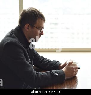 Verärgert depressiven russischen Mann nachdenklich auf die Seite. Papiertasse Kaffee in den Händen. Traurigkeit und Verzweiflung Konzept Stockfoto